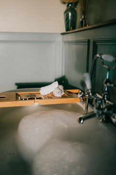 Bubbly bathtub with wooden tray holding rolled towels and bath items. Soft lighting adds warm, relaxing ambiance. Ideal for spa, wellness, or luxury bathroom themes