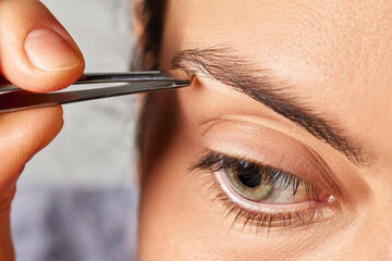Woman grooming her eyebrow with tweezers, removing unwanted hair for precise shaping