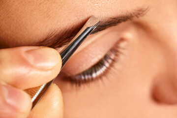 Close-up of person's hand using tweezers to remove stray eyebrow hairs near eye