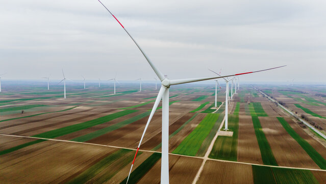 Aerial view of towering wind turbines stand as guardians over the patterned fields, their stark white forms contrasting against the earthy hues, Alibunar, Vojvodina, Serbia.
