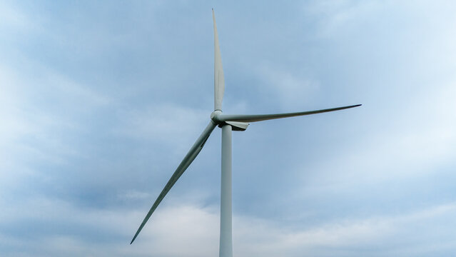 Aerial view of a solitary wind turbine standing tall against a backdrop of soft, cloudy skies, its stark white contrasting with the muted tones, Alibunar, Vojvodina, Serbia.