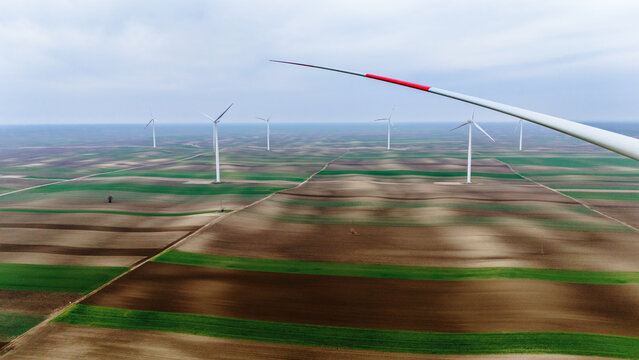Aerial view of wind turbines standing tall over the patchwork of fields, a symphony of greens and browns under a soft, diffused light, Alibunar, Vojvodina, Serbia.