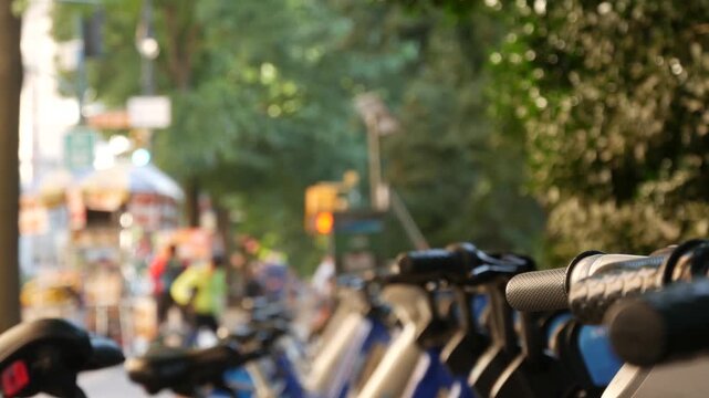 Manhattan Midtown street New York City, United States. Rental bicycle parking on Central Park West, trees summer greenery. Bike for rent in row. Defocused people pedestrian on sidewalk pavement.