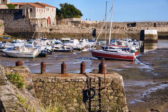View of boats resting on the muddy banks under a clear sky, with a stone fortress standing guard in the background, Saint-Jean-de-Luz, Nouvelle-Aquitaine, France.