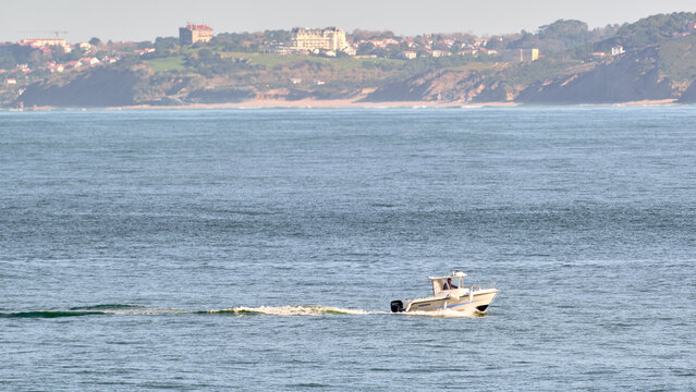 View of a motorboat glides across the tranquil sea, leaving a trail of white foam against the backdrop of the coastal town, Saint-Jean-de-Luz, Nouvelle-Aquitaine, France.