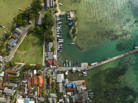 Aerial view of boats docked at the pier, contrasting with the clear turquoise waters and the town's red-tiled roofs, Karimunjawa, Central Java, Indonesia.