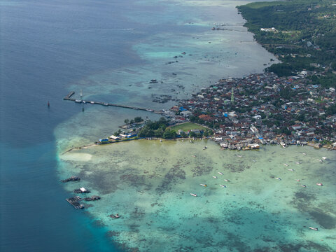 Aerial view of a vibrant coastal town where the turquoise waters meet the dense buildings near Karimunjawa Town Square, Karimunjawa, Central Java, Indonesia.