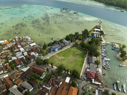 Aerial view of the vibrant town square meeting the turquoise sea, where boats bob gently and houses cluster tightly, Karimunjawa, Central Java, Indonesia.