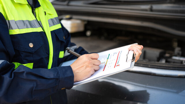 A technician is checking on car inspection checklist form to verify the safety condition after serviced. Industrial working scene, close-up and selective focus. 