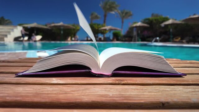 An open book on a lounger by the pool in luxury resort or hotel on a peaceful, sunny day. Vertical, slow motion view and copy space for text.