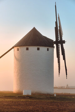 View of a solitary white windmill with striking black sails stands proudly against the soft, pastel hues of dawn's embrace, Campo de Criptana, Castile-La Mancha, Spain.