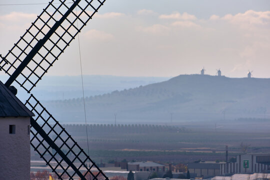 View of towering windmills cast long shadows on the land, the distant silhouettes of more windmills atop a hill, Campo de Criptana, Castile-La Mancha, Spain.