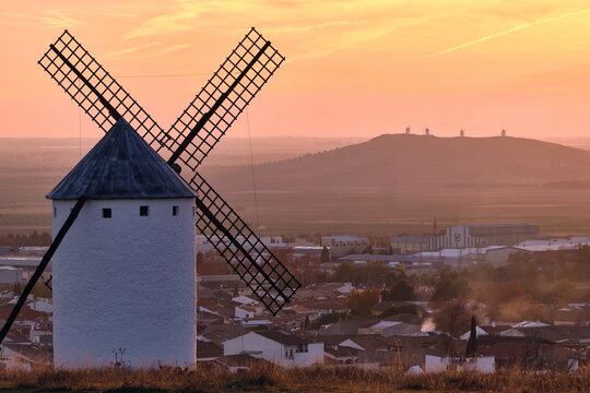 View of a white windmill standing tall against a pastel sunrise, overlooking the village and distant windmills on a hilltop, Campo de Criptana, Castile-La Mancha, Spain.