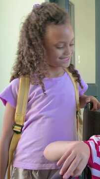 Vertical video: Facing camera girl fixing yellow pack near door touching wheelchair helping friend