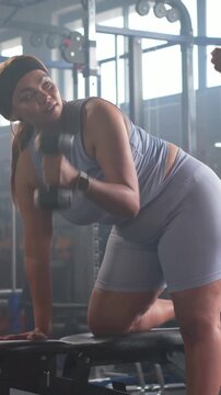 Vertical video: Pulling weight bracing left knee and hand on bench woman in blue coach aiding form