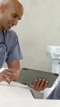 Vertical video: Staff asking medic in scrubs rotating tablet at clinic desk tapping app with steth