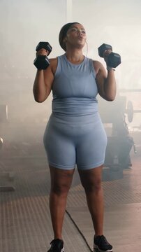 Vertical video: Starting, woman in blue set raising then pressing hex dumbbells in gym for strength