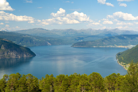 View of serene lake by Innvik Fjord reflecting the sky and surrounding mountains, framed by lush green trees, creating a tranquil scene, Utvik, Vestland, Norway.