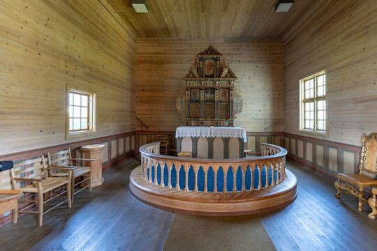 View of rustic wooden church interior with intricate altar, bathed in warm light streaming through windows, creating a serene atmosphere, Utvik, Vestland, Norway.