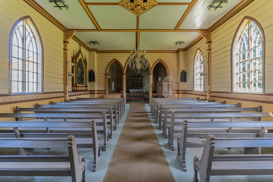 View of symmetrical rows of pews lead toward the altar in a light-filled wooden church interior, a serene haven of faith and architectural detail, Utvik, Vestland, Norway.