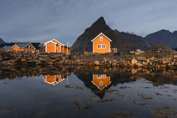 Stunning fall scenery in the Lofoten Islands. Iconic red rorbu cabins nestled between rocky coastlines and dark arctic waters during the golden hour. Travel Norway. © PawelUchorczak