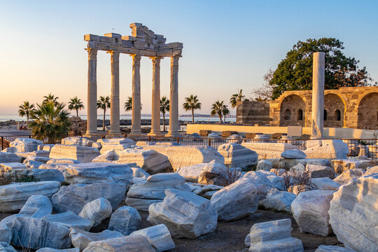 Ancient Temple of Apollo ruins with tall Corinthian columns and marble blocks in golden sunset light. Historical archaeological site in Side resort under clear sky. Antalya region, Turkey.