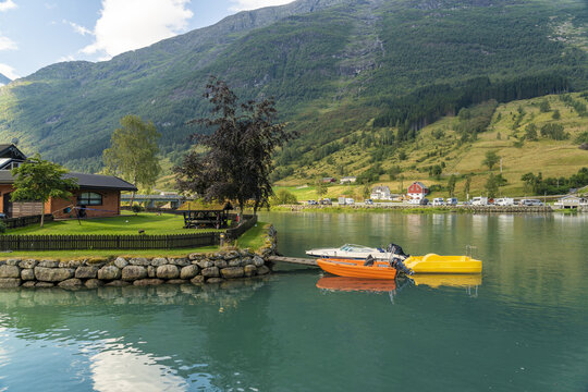 View of tranquil waters reflecting the lush green mountains as colorful boats bob gently near quaint houses, a serene escape, Olden, Vestland, Norway.