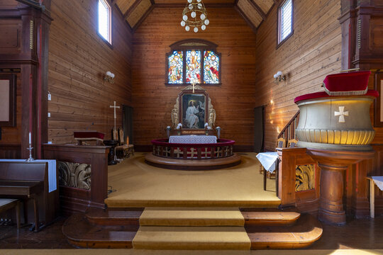 View of the Olden Old Church's wooden interior, bathed in soft light filtering through stained glass, contrasts with the rich, dark wood paneling, Olden, Vestland, Norway.