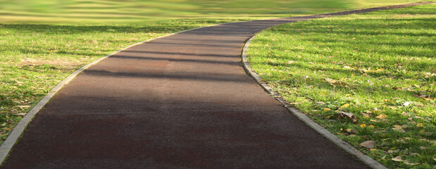 Fototapeta premium Perspective view of the city park with curved sporty empty road with brown surface green grass for bicycle ride and jogging paths. summer spring landscape with empty public garden. mockup template