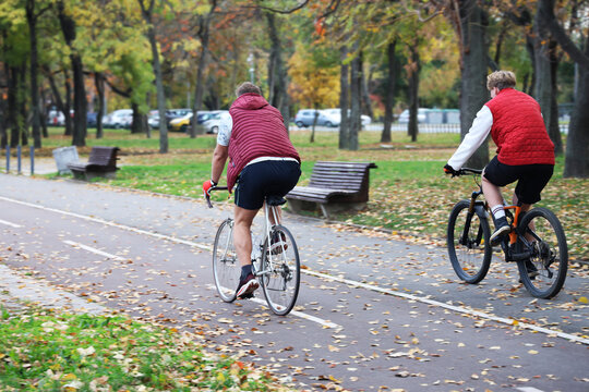 Stylish couple of middle age couple people ride in autumn seasonal fall season park during the autumn season at sunset. Active cycling in park on the weekend. Back rear view. Belgrade Serbia Usce park