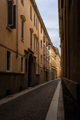 Fototapeta premium Cinematic view through a monumental stone archway looking down the narrow cobbled street of Borgo Angelo Mazza in Parma, Italy 06.01.2026