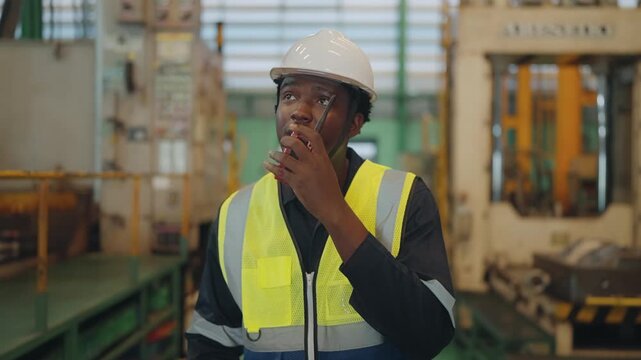 Young African male mechanical technician or engineer using a two-way radio to give instructions while walking in an industrial factory