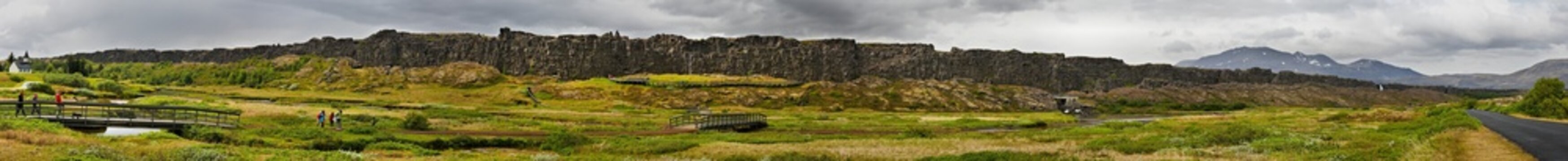 Thingvellir - Iceland Panoramic view of Thingvellir, Iceland, showcasing a dramatic landscape with rocky cliffs and expansive grassy plains.