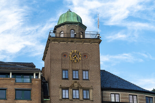 View of an old clock tower with a distinctive green dome rises against a bright blue sky streaked with wispy clouds, Bergen, Vestland, Norway.