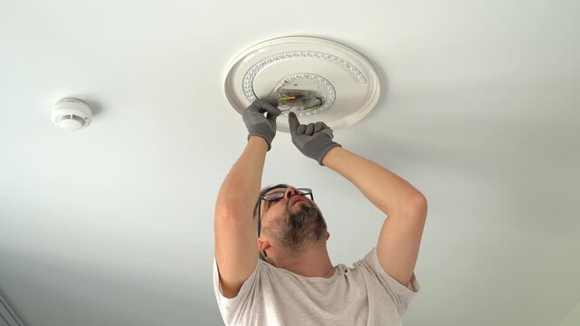 Electrician installs ceiling LED lamp on suspended ceiling at home. Hands connect wires of lamp frame. Installation light