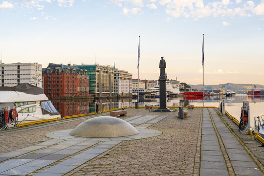 View of the calm waters reflect the colorful buildings on the opposite shore near a stone dome and statue, Bergen, Vestland, Norway.