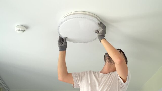 Electrician installs ceiling LED lamp on suspended ceiling at home. Hands connect and fix lampshade. Installation light