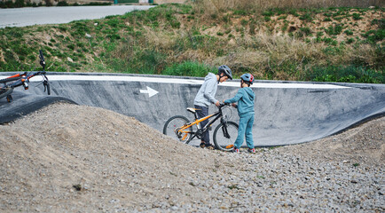 Obraz premium Brother helping younger sibling with bicycle on pump track