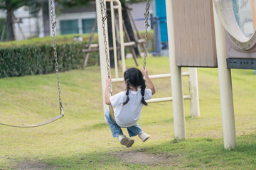 Joyful Child Swinging on Playground Swing in Sunny Park, Enjoying Outdoor Fun and Freedom in Simple White T-shirt and Blue Jeans
