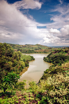 View of a tranquil lake nestled between rolling green hills covered in lush vegetation under a sky with scattered clouds, Kampala, Central Region, Uganda.