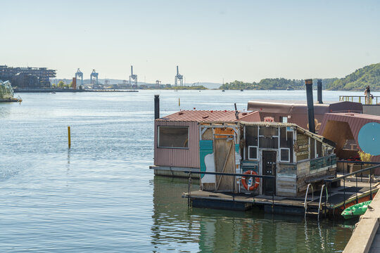 View of weathered houseboats with vibrant colors and textures drift on the calm water under a clear sky, with industrial cranes in the distance, Oslo, Oslo, Norway.