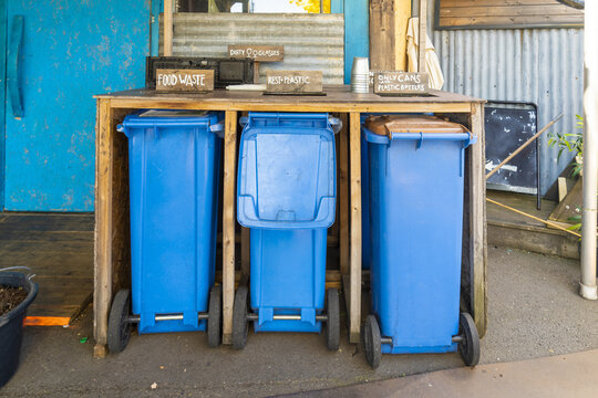 View of three blue recycling bins, labeled for food waste, mixed waste, and recyclables, sit neatly under a wooden frame, Oslo, Norway.
