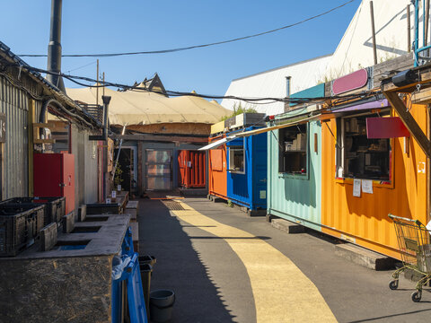 View of vibrant, repurposed shipping containers transformed into food stalls under a clear blue sky, creating a lively urban scene, Oslo, Oslo, Norway.