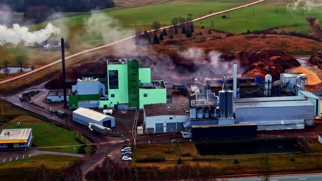 Aerial view of a factory with a smoking chimney, next to a pile of steaming pulp.