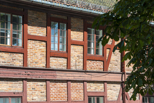 View of the rich, textured brick and timber facade of a building, framed by the vibrant green foliage of a tree, Oslo, Oslo, Norway.