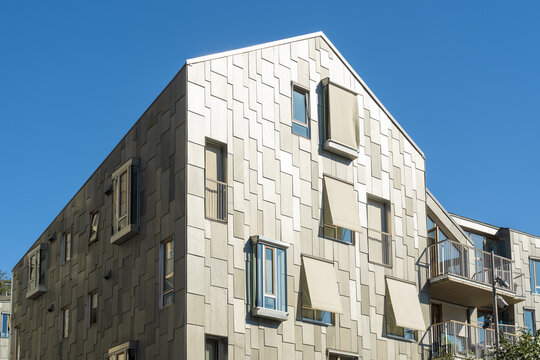 View of a modern apartment building with a unique facade under a clear blue sky, casting shadows on the textured walls, Oslo, Oslo, Norway.
