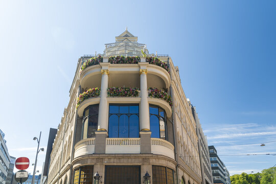 View of an ornate building with a glass-enclosed upper level adorned with flowers under a vast blue sky, Oslo, Oslo, Norway.