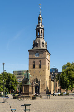 View of sunny Stortorvet square with Christian IV Statue featuring Oslo Cathedral's towering steeple, surrounded by vibrant green trees and market stalls, Oslo, Oslo, Norway.