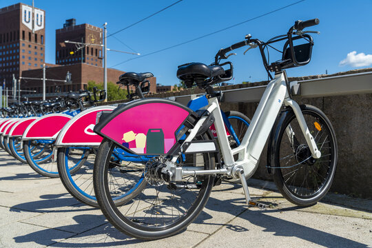 View of electric bicycles lined up on a bright sunny day, contrasting pink and white against the city hall's brick facade, Oslo, Oslo, Norway.