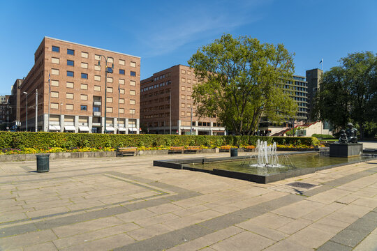 View of tranquil fountain reflecting the sky, framed by brick buildings and lush greenery in a serene urban scene, Oslo, Oslo, Norway.